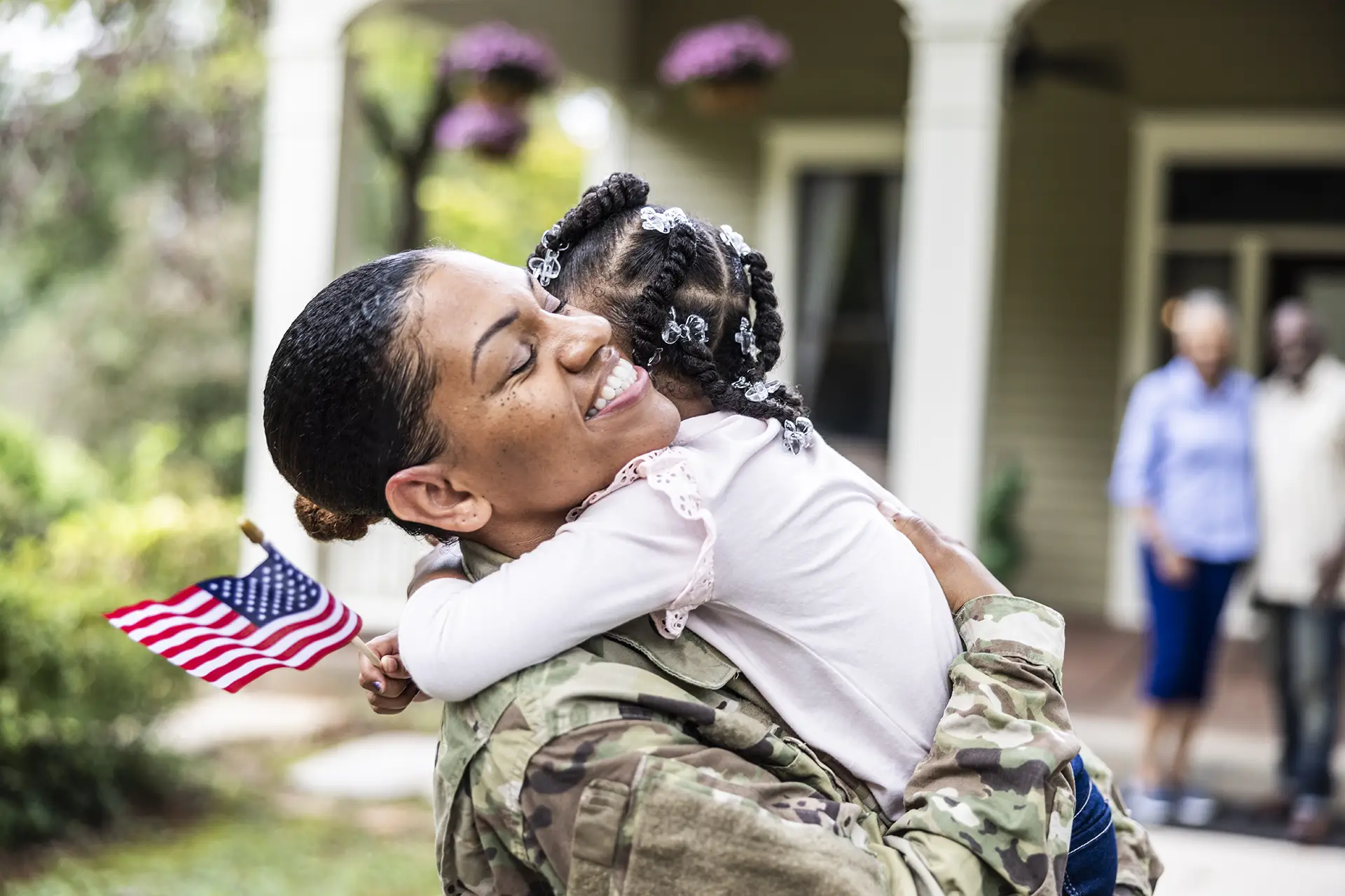 Daughter embracing female U.S. soldier mother in front of home